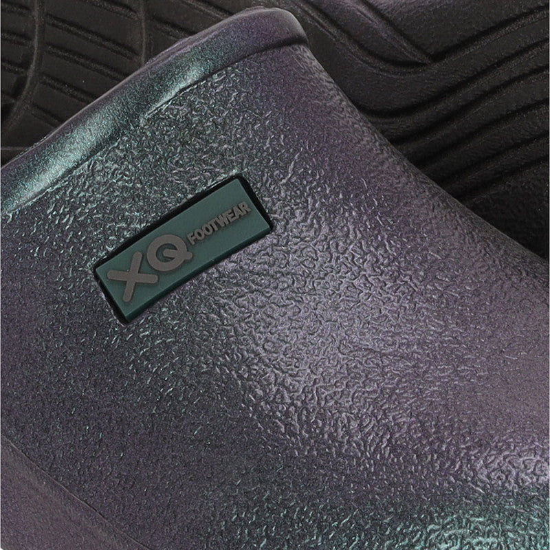 Close-up van XQ Tuinklompen Dames Parelmoerglans Zwart, een instapmodel gemaakt van lichtgewicht EVA-kunststof met antislip zool en subtiele eikel; voorzien van het XQ Footwear-label, met een andere schoen deels zichtbaar op de achtergrond.