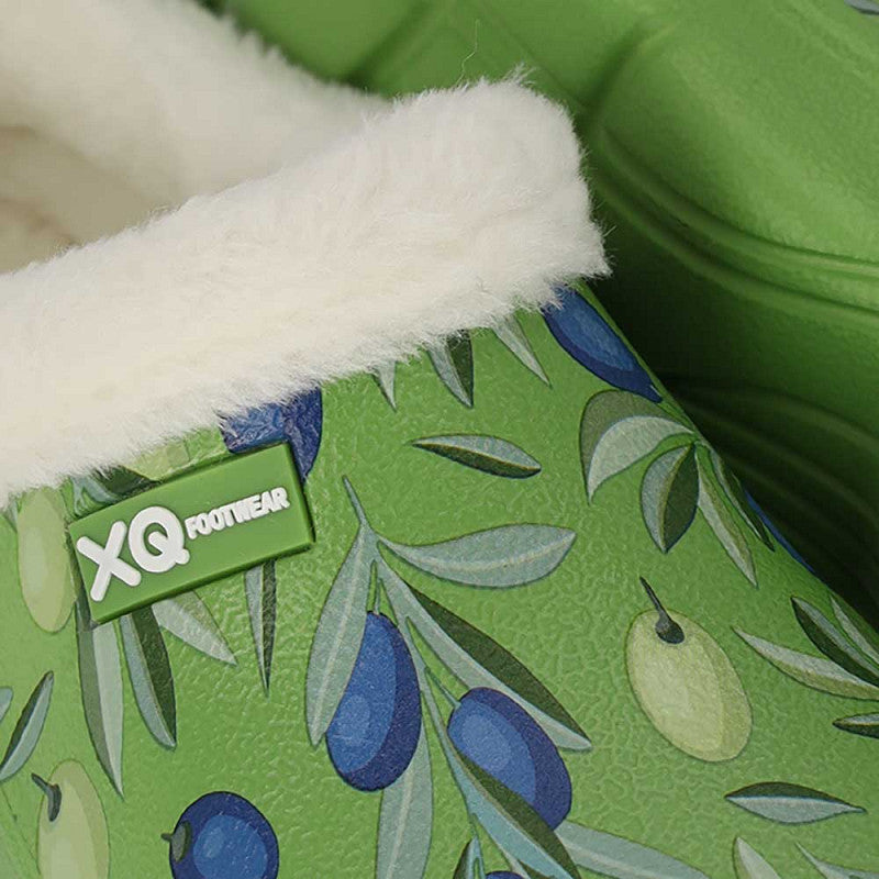 Close-up van een groen XQ Tuinklompen Dames slofje met zachte, warme voering en een olijvenprint in blauw en groen. De pantoffel heeft een groen label met de naam XQ FOOTWEAR.