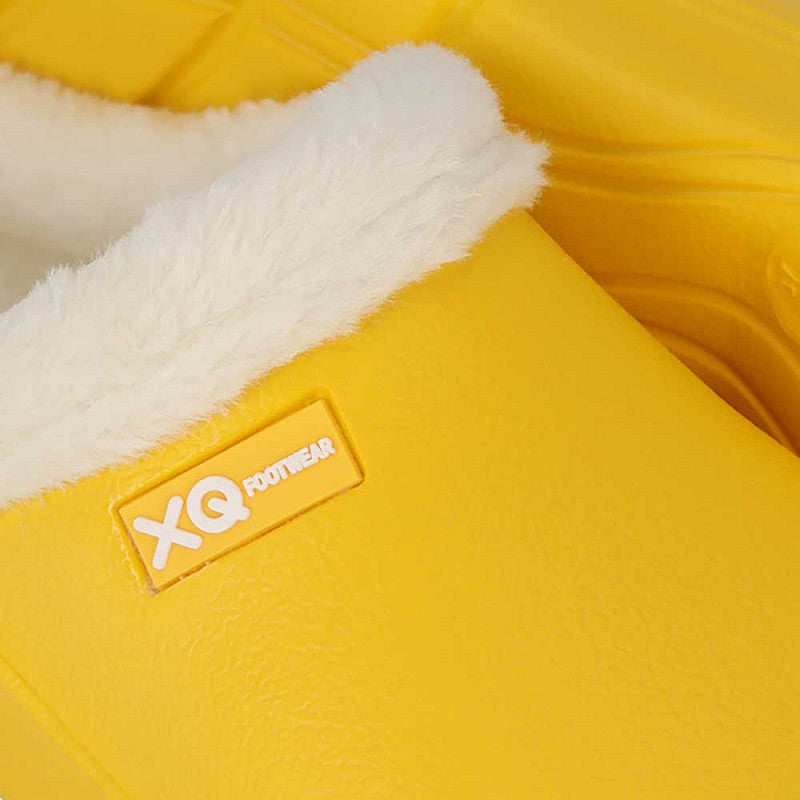Close-up van de XQ Tuinklompen Dames Met Bontje Fashion - Geel pantoffel met witte, donzige voering en een XQ FOOTWEAR label. De antislip zool biedt een stevige ondergrond, tegen de achtergrond van gezellig materiaal.