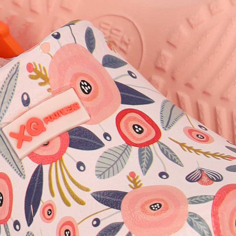 Close-up van de XQ Tuinklompen Meisjes met klittenband, met een kleurrijke bloemenprint in roze, rood en groen. Het XQ FOOTWEAR-label is zichtbaar en de deels roze zool heeft een antislip zool voor extra grip.