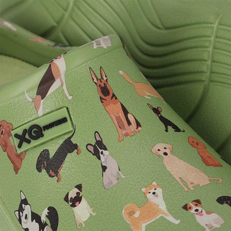 Close-up van de XQ Tuinklompen Dames met Dierenprint - Honden, een groene tuinklomp versierd met speelse illustraties van hondenrassen en met een XQ Footwear-label op de zijkant.