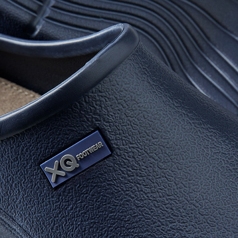 Close-up van het XQ Tuinklompen Heren Navy instapmodel in donkerblauw, met waterafstotend materiaal, gedetailleerde stiksels, een klein XQ Footwear-label op de zijkant en een lichtgewicht gebogen ontwerp.