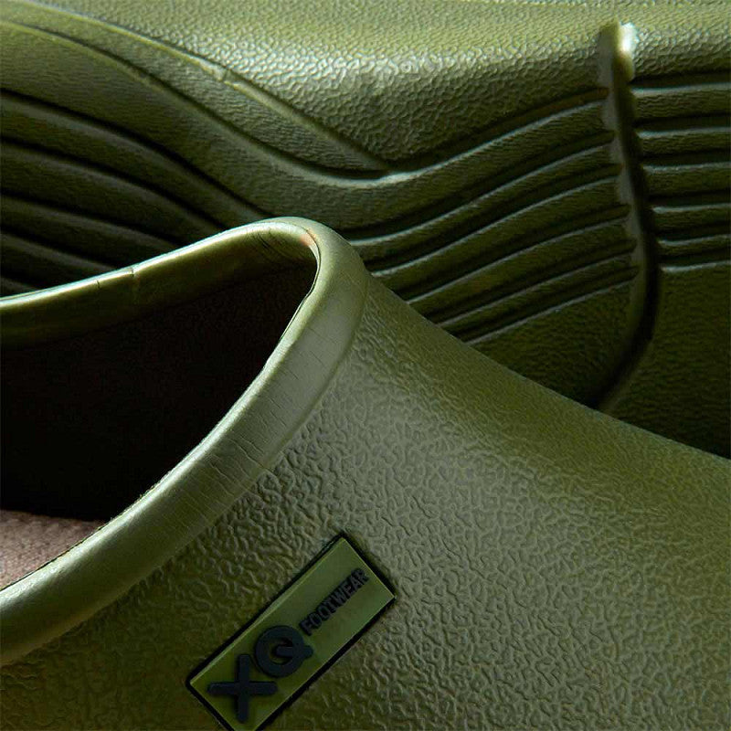 Close-up van XQ Tuinklompen Heren Olijfgroen - Instapmodel & Lichtgewicht met het groene structuurrubber, het XQ Footwear-label en de geribbelde waterafstotende zool op de achtergrond.
