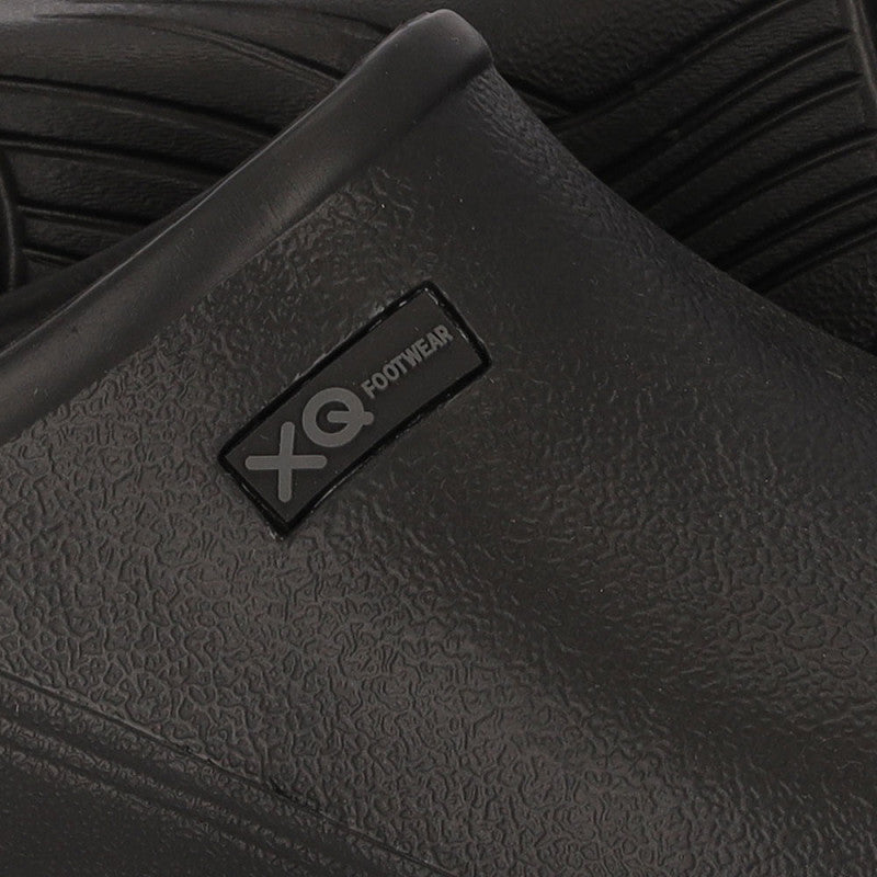 Close-up van de XQ Tuinklompen Heren Zwart - Instapmodel & Lichtgewicht, een zwarte, waterafstotende slip-on van lichtgewicht EVA-kunststof met een XQ FOOTWEAR-label; op de achtergrond staat een andere klomp met een gegroefde zool.