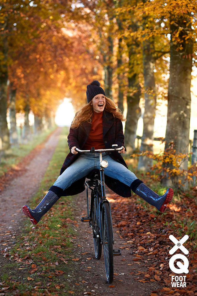 Vrouw op de fiets met regenlaarzen in een herfstlaan
