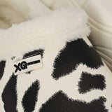 Een close-up van de XQ Tuinklompen Dames met Bontje & Koeienprint: gezellige pantoffels met warme voering, zwart-witte koeienprint en een label met XQ FOOTWEAR - perfect voor fans van klompen met koeienprint.