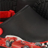 Een close-up van de XQ Tuinklompen Jongens, een zwarte klompschoen voor kinderen met LED-lampje, met een Formule 1-print raceauto op de zijkant, rode band en zwarte zolen met textuur op de achtergrond.