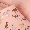 Close-up van de met Dierenprint - Paarden XQ Footwear sandaal in roze, met rennende paarden in bruin, wit en bruin. De waterafstotende tuinklompen liggen op een getextureerde roze achtergrond.