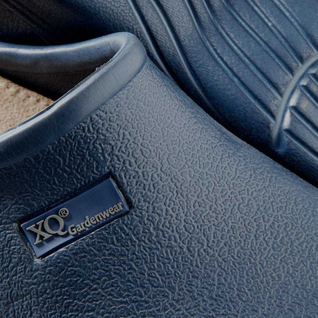 Close-up van XQ Tuinklompen Dames Navy - Instapmodel & Lichtgewicht, met blauw structuur oppervlak en XQ Gardenwear-label. Eén klomp is gedeeltelijk gestapeld, waardoor het profielpatroon op de zool zichtbaar is.
